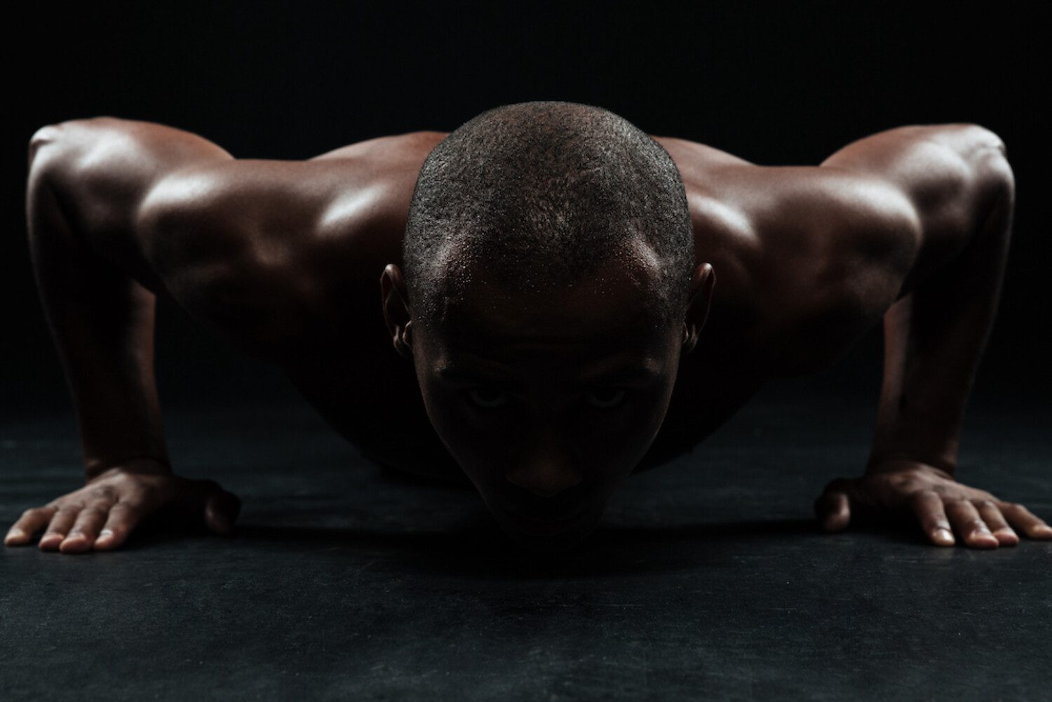 Close-up portrait of afro american sports man, doing pushup exercise in black interior